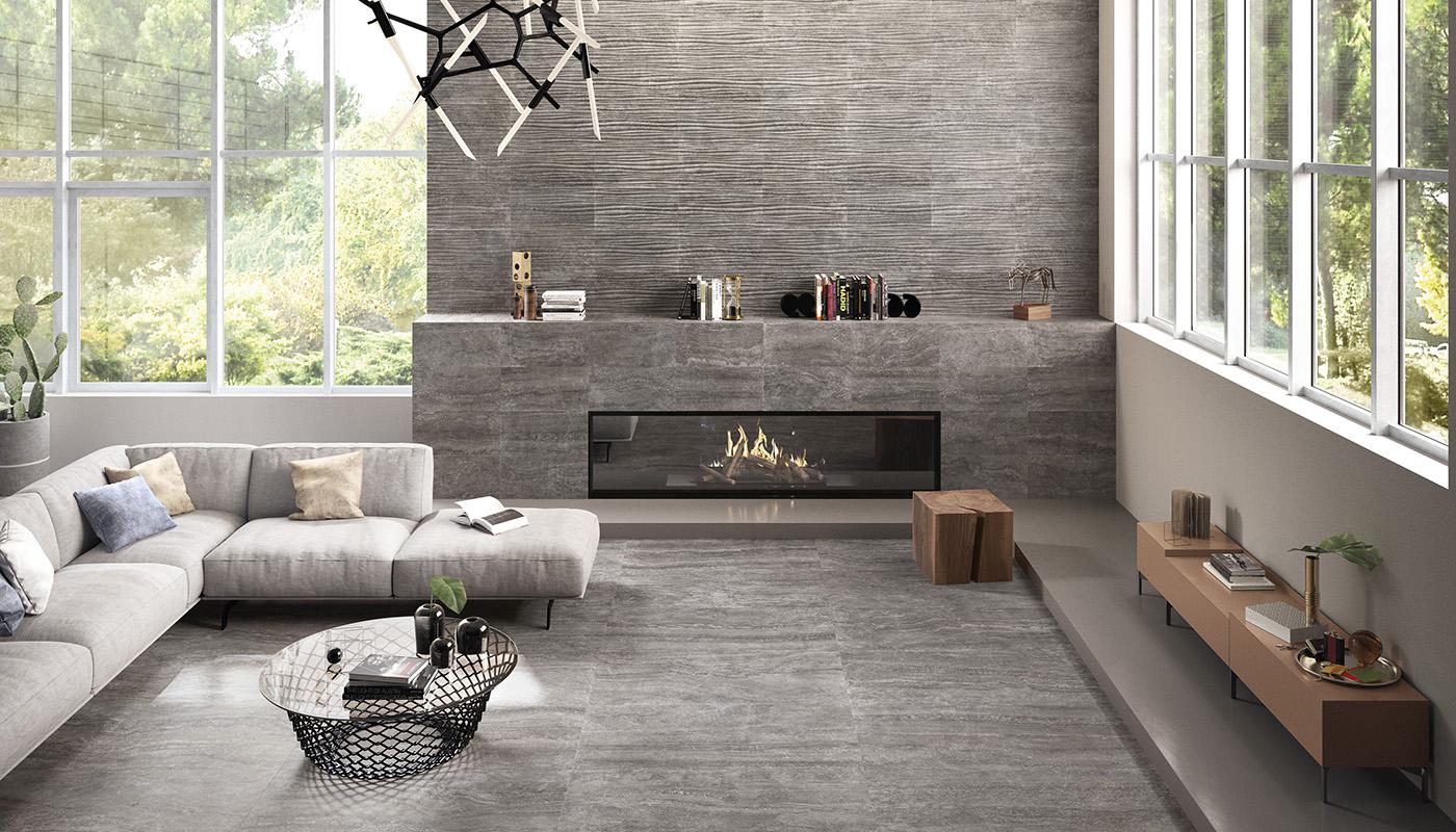 Alt text: "Modern living room featuring Emilceramica Eterna Italian porcelain tile collection with a sleek grey design on floors and walls, complemented by a contemporary sofa, glass coffee table, and a cozy fireplace."