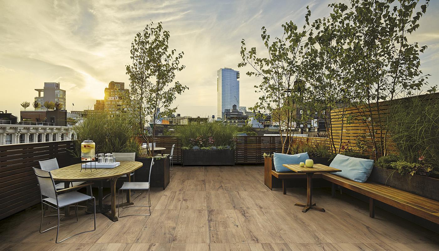 Modern rooftop terrace with Emilceramica Millelegni porcelain tile flooring showcasing wood effect, outdoor furniture, and city skyline view