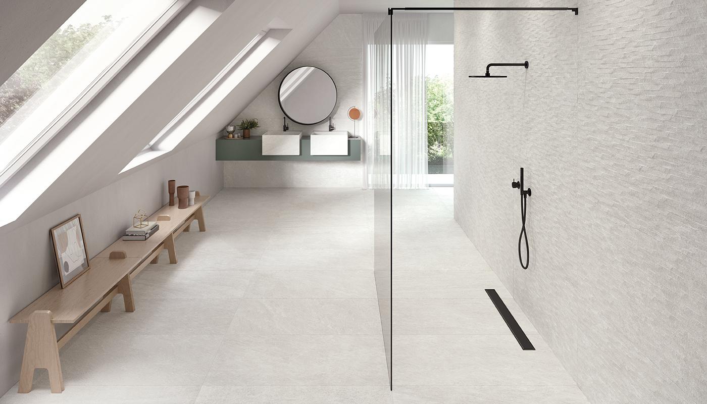 Elegant modern bathroom with Emil Ergon Oros Stone Italian porcelain tile flooring and textured wall, featuring skylight, glass shower, and minimalist decor.