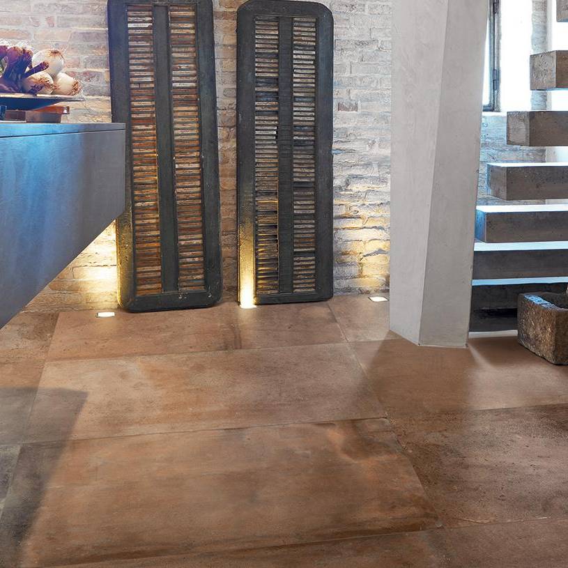 Alt text: Warm terracotta tones of porcelain tile flooring in a modern interior with decorative lighting and stairway, showcasing the ceramic-like finish and texture.
