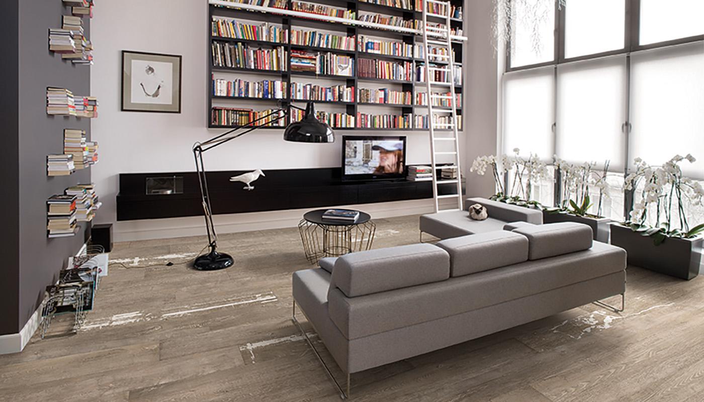 Modern living room with Emil Viva Statale 9 porcelain tile flooring, featuring a grey sofa, floor-to-ceiling bookshelf, and large windows