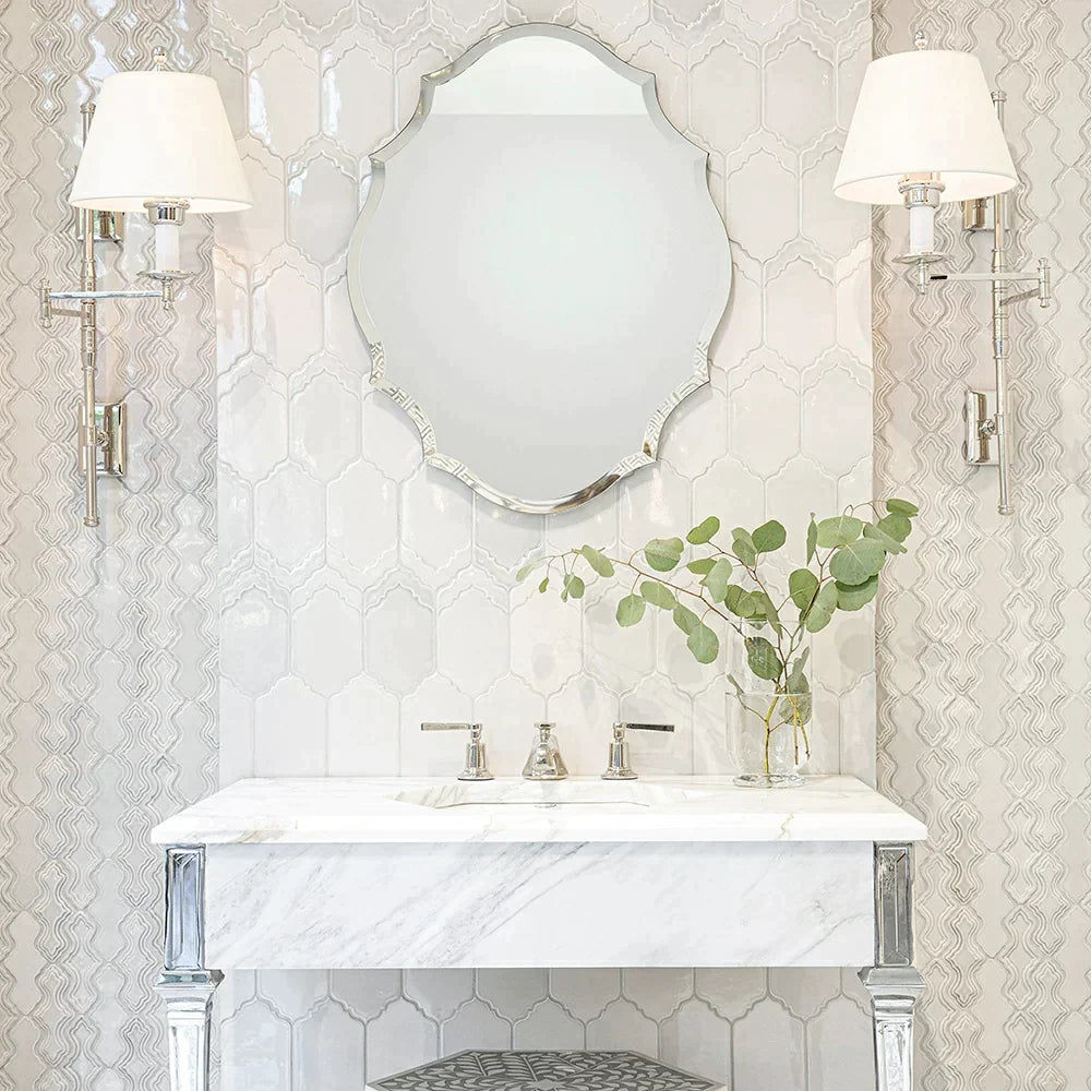 Elegant bathroom featuring the Breathe Moresque ceramic tile collection with intricate arabesque patterns on the wall, marble countertop, classic silver mirror, and sophisticated wall sconces.