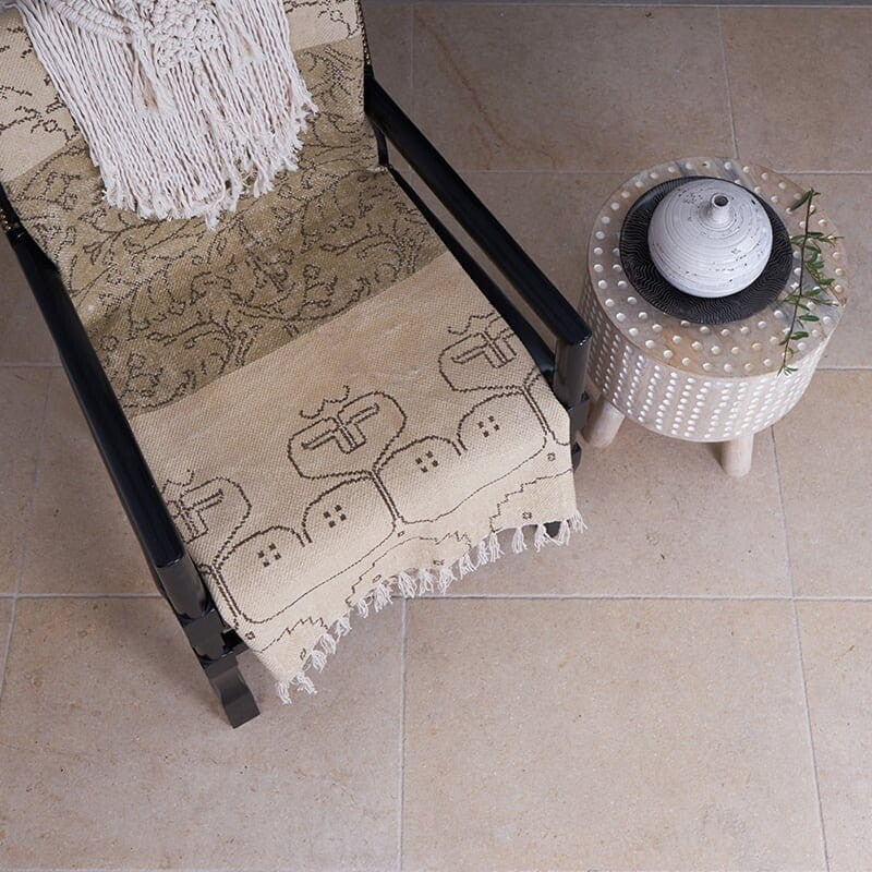 Cozy room with beige marble tile flooring, black chair with beige throw blanket, small white side table with decorative vase and green twig.