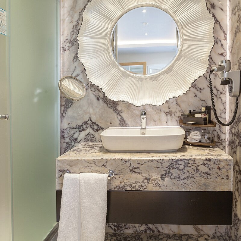 Luxurious marble bathroom with gray veining, modern white sink, round mirror, and white towel hanging.