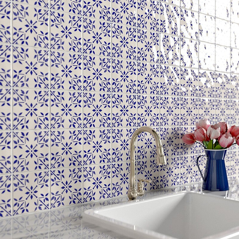 Blue and white square tiles on wall with silver faucet; navy blue vase with flowers on right of sink.