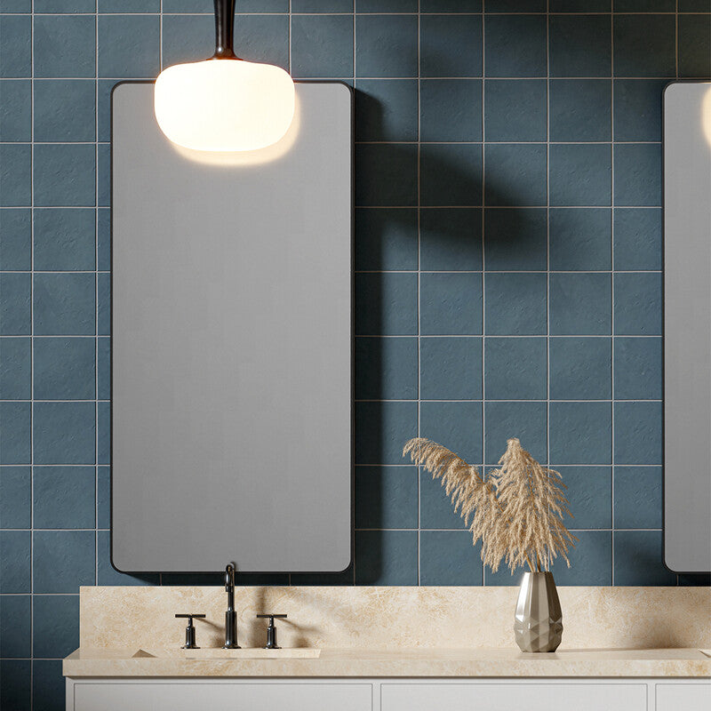 Modern bathroom with blue square tiles, rectangular mirror, white countertop, stainless steel faucet, and silver vase with dried pampas grass.