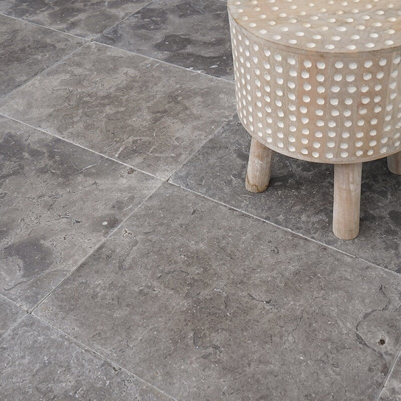 Beige wooden stool with white polka dots on gray marble floor with beveled edge.