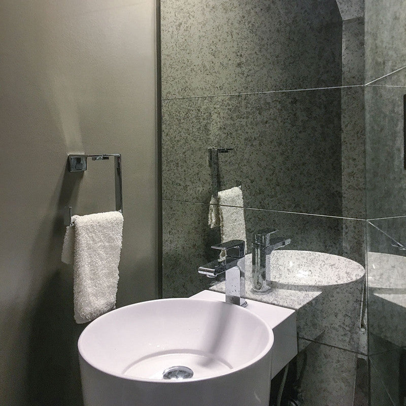 Modern bathroom with gray antique mirror tiles, round white vessel sink, chrome faucet, white towel on chrome towel ring.