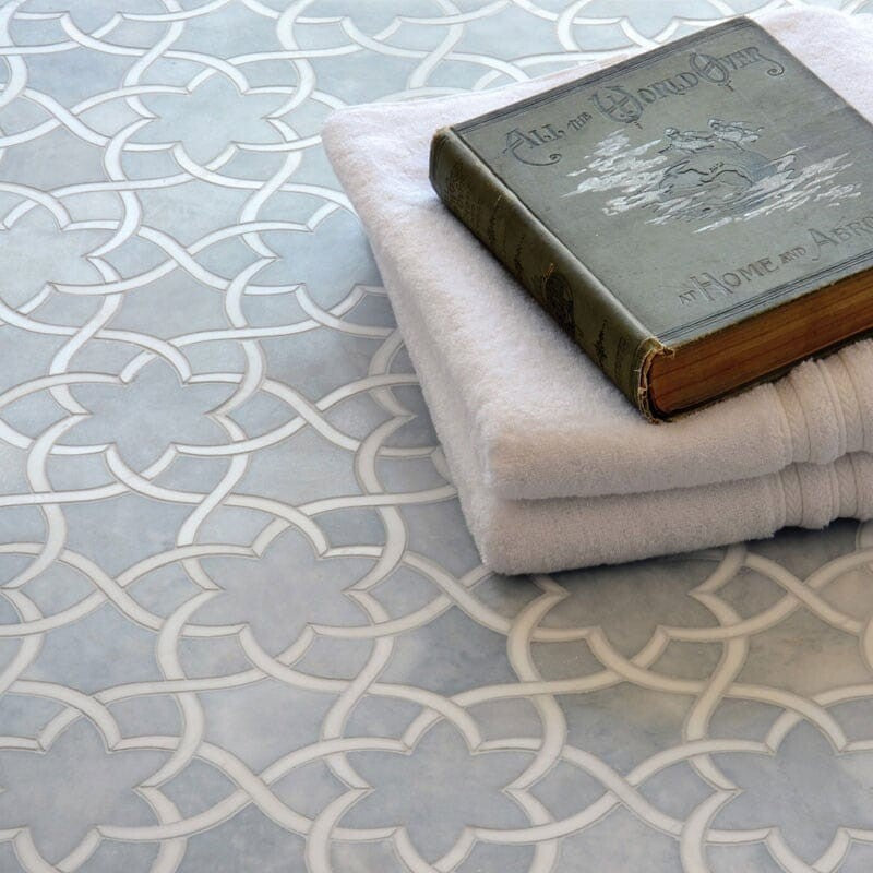 Detailed grey and white mosaic pattern with geometric designs, vintage book, and folded towel on top.
