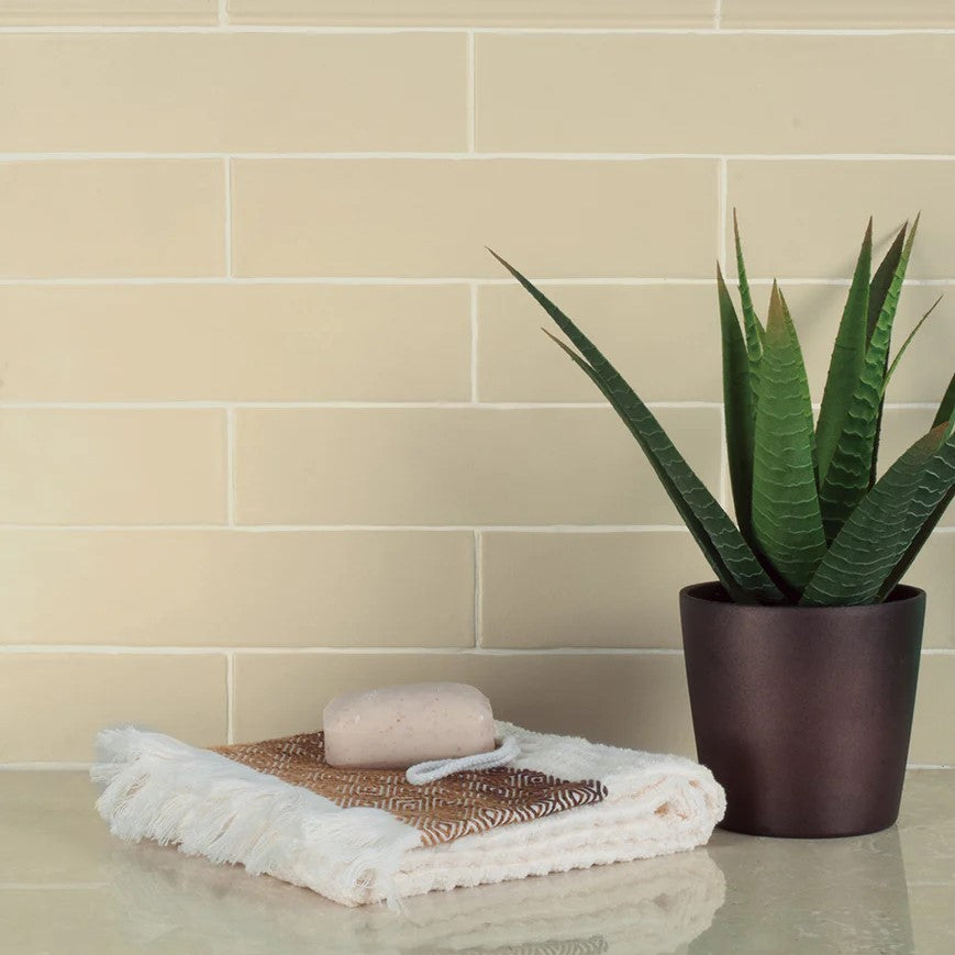 Subtle cream-colored Adex Earth Ceramic Tiles with a gentle crackle finish displayed as a backsplash, complemented by a potted aloe vera and a stack of spa essentials, embodying a natural and calming aesthetic.