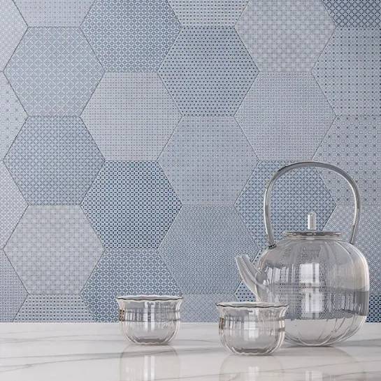 Hexagon-patterned porcelain tiles in varying shades of blue and gray with a reflective silver teapot and cups on a white surface.